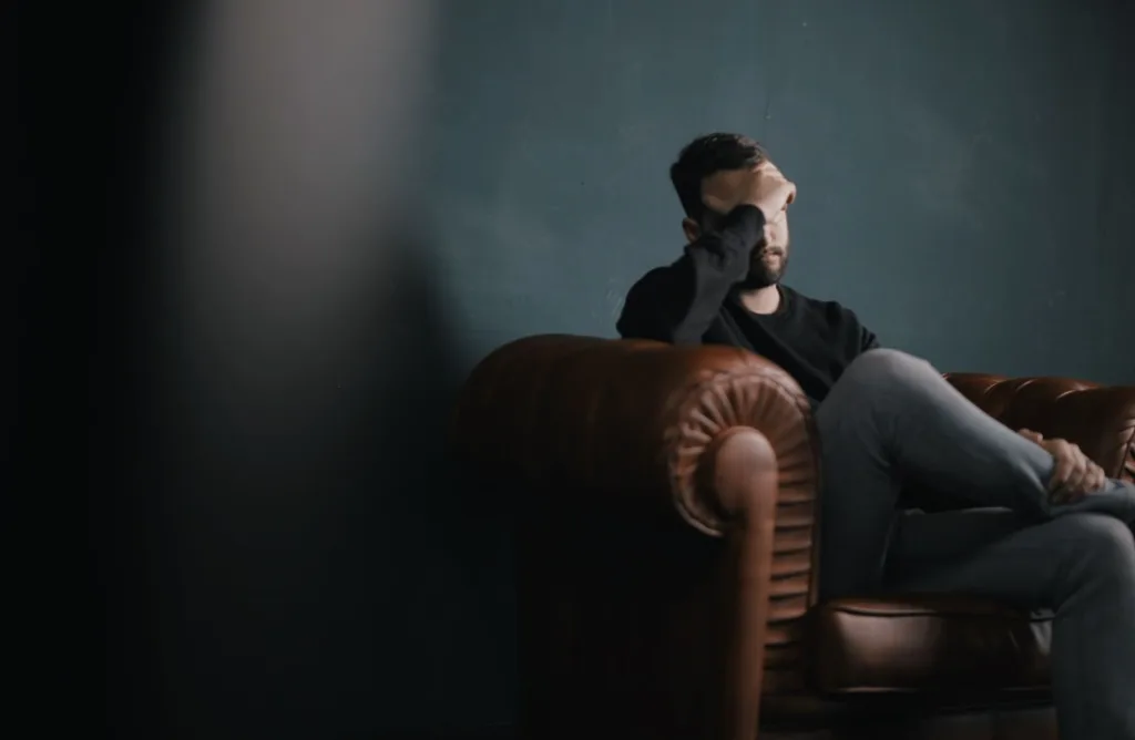 a man holds his head while sitting on a sofa, streaming anxiety