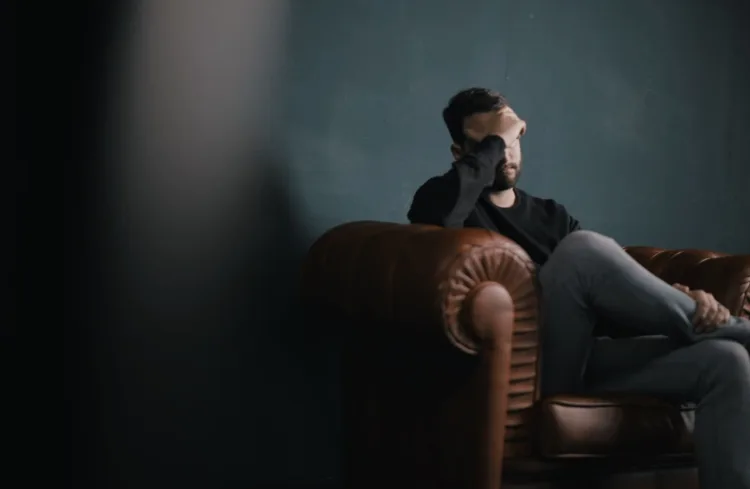 a man holds his head while sitting on a sofa, streaming anxiety