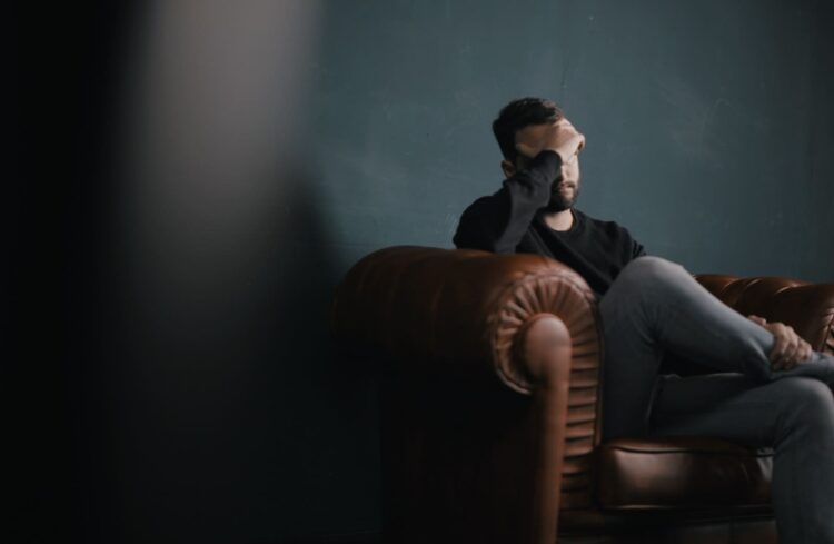 a man holds his head while sitting on a sofa, streaming anxiety